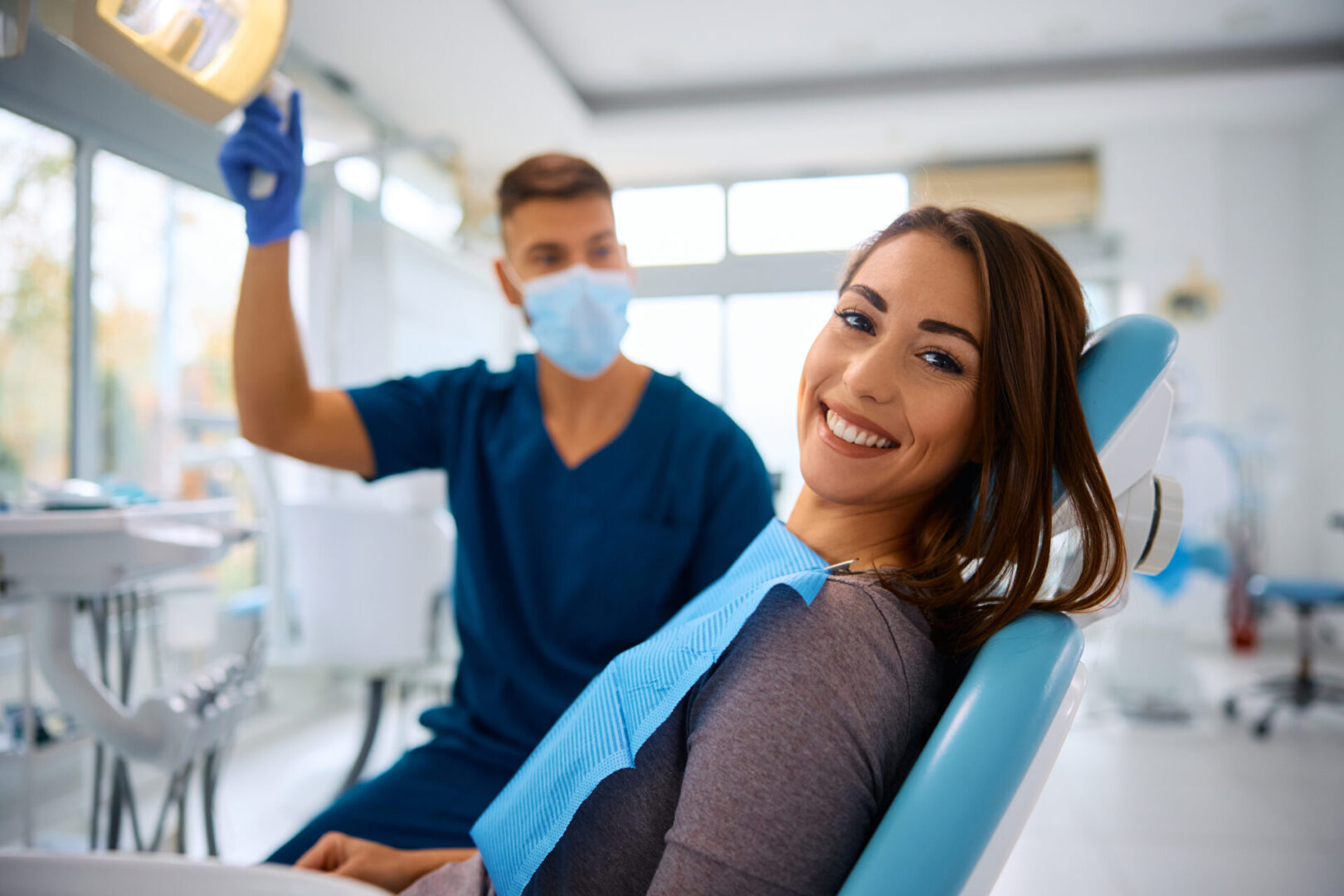 A woman smiling in a dental chair with a dentist in the background.