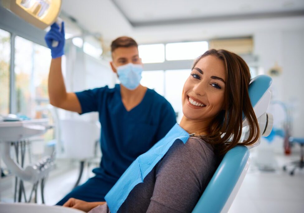 A woman smiling in a dental chair with a dentist in the background.