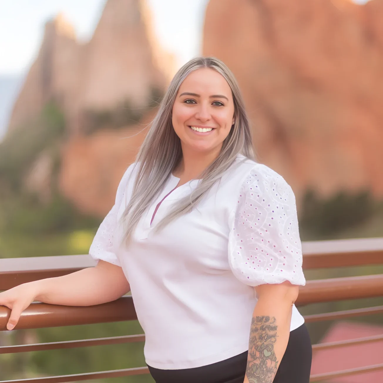 Smiling woman posing outdoors with rocky formations in the background.