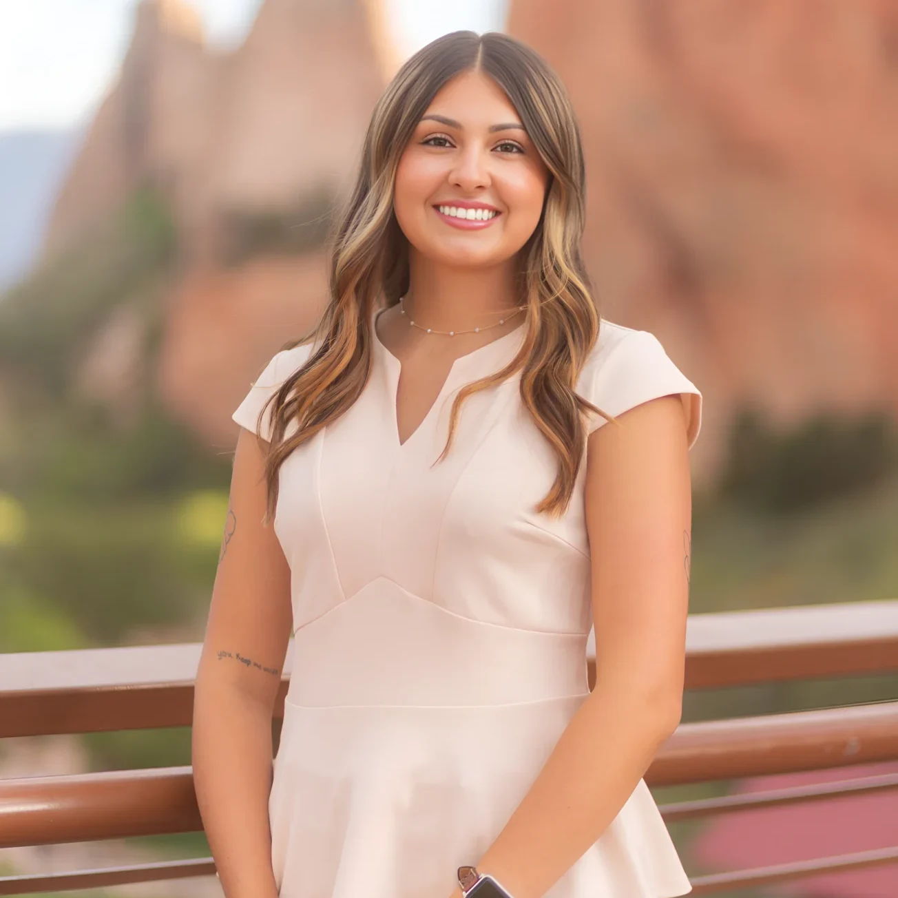 A smiling woman in a white dress outdoors with natural scenery.