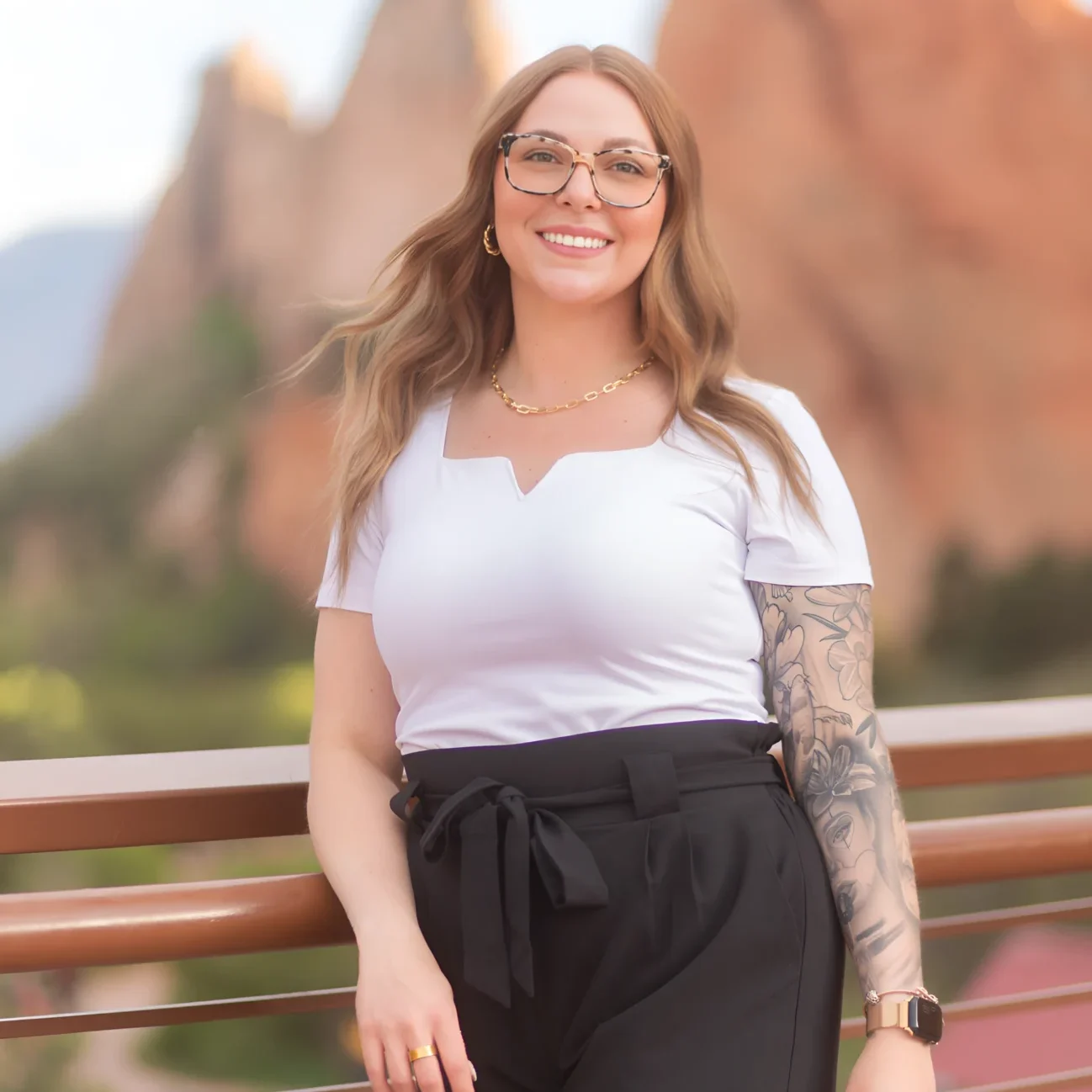 Young woman with glasses smiling outdoors near red rock formations.
